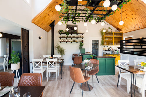 Bright dining room filled with plants. A wood ceiling, green cupboards. Tables are set for a fine dining experience.